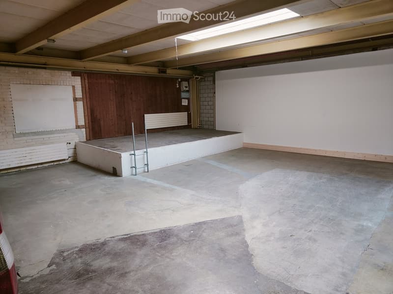 Empty room with concrete floor, white walls, raised platform, and wooden paneling on one side.