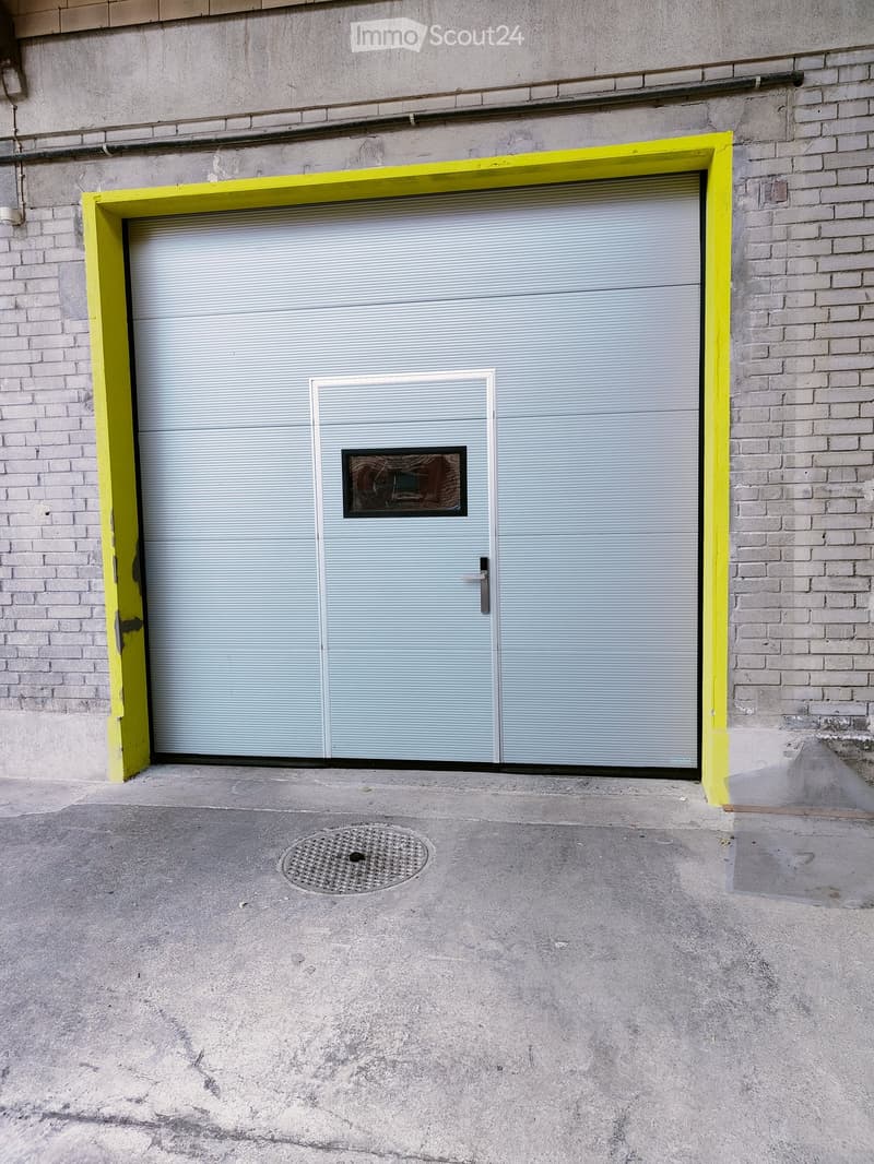 A large industrial-style garage door with a small access door, set in a brick building with a concrete ground.