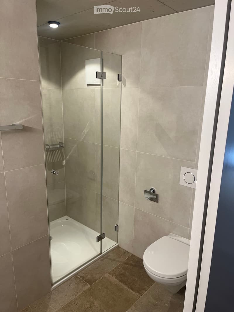 Modern bathroom with a glass-enclosed shower, a toilet, and a bathtub, featuring beige tiles and a sleek design.