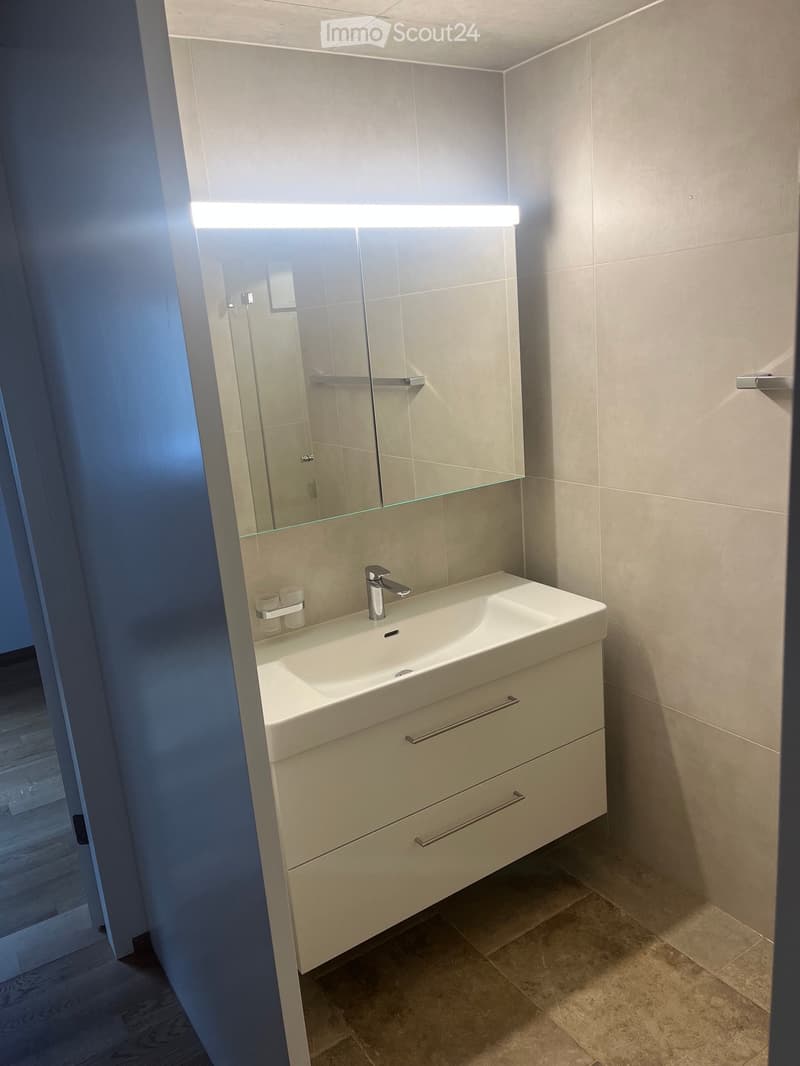 Modern bathroom with a white sink, chrome faucet, mirrored cabinet, and two cups on the counter.