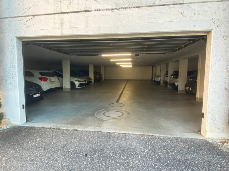 Underground parking area with several parked cars, concrete floors, and white walls.