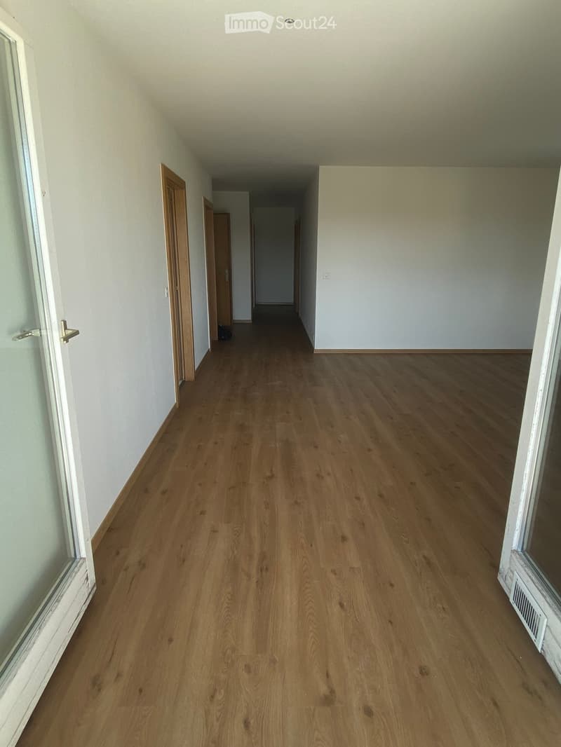 Empty hallway with wooden flooring, white walls, and doors on both sides.