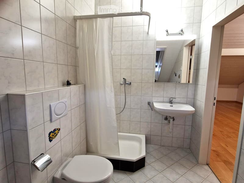 Modern bathroom with white tiles, a toilet, a sink, a mirror, and a shower with a curtain.