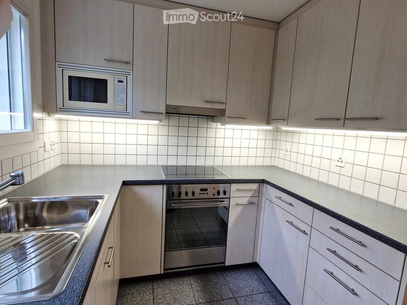 Modern kitchen with light wood cabinets, stainless steel appliances, and a tiled backsplash.