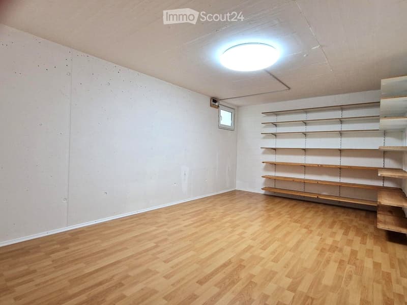 Empty room with wooden flooring, white walls, built-in wooden shelves, and a small window.