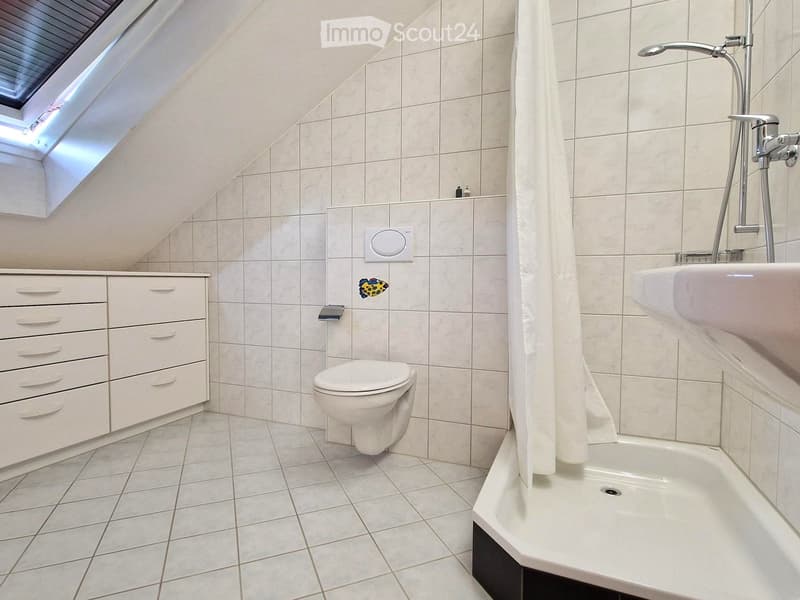 Modern bathroom with white tiles, a toilet, a sink, a bathtub, and a cabinet with drawers. A skylight window provides natural light.