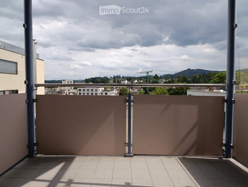 Balcony with tiled floor, metal railing, and brown privacy screens, overlooking a cityscape with buildings and greenery.