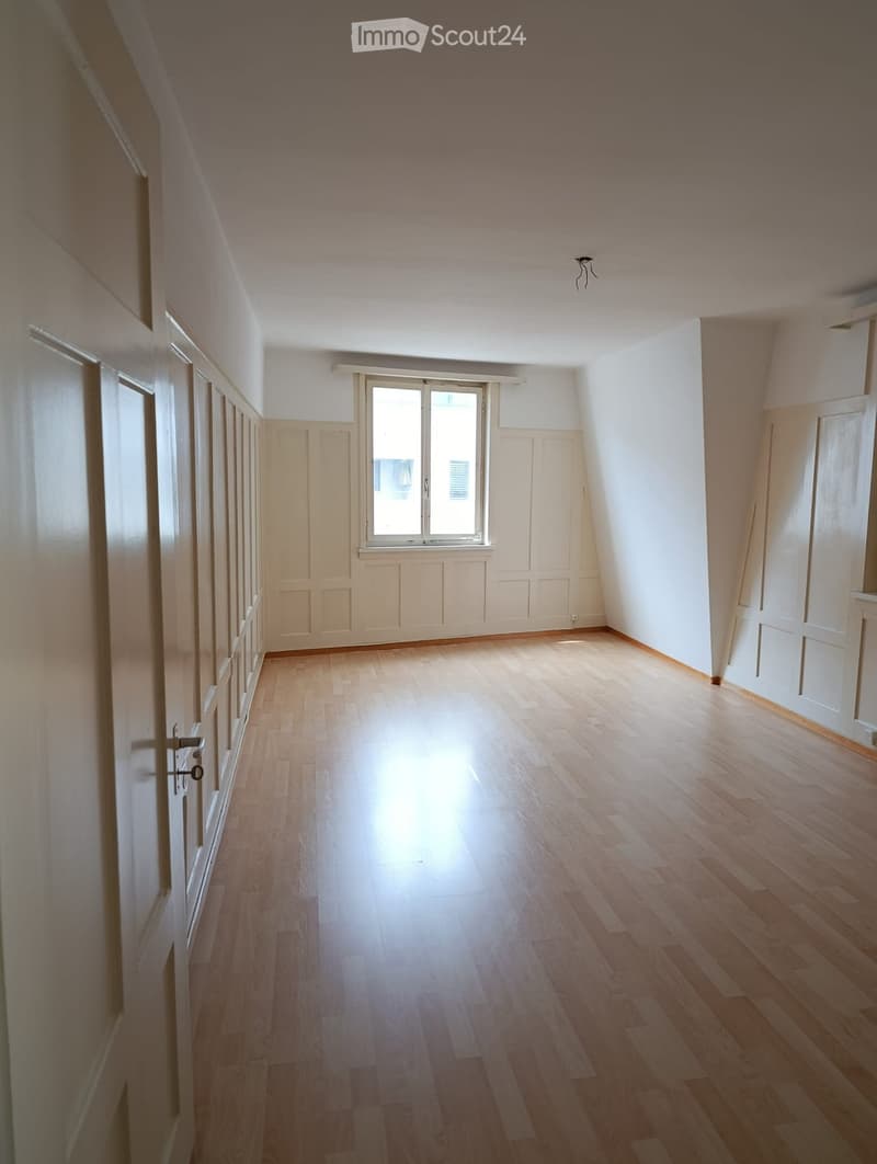 Empty hallway with wooden flooring, white walls, and a large window at the end allowing natural light to enter.