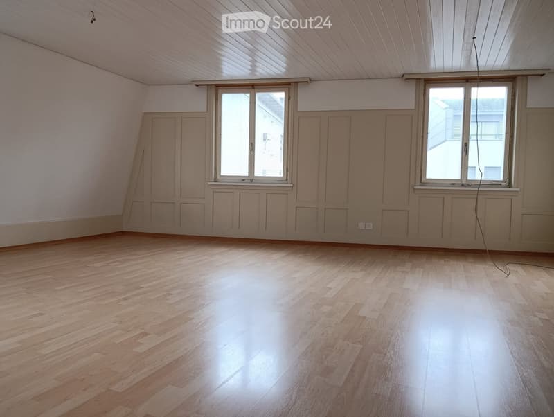 Empty room with wooden flooring, white walls, and large windows allowing natural light.