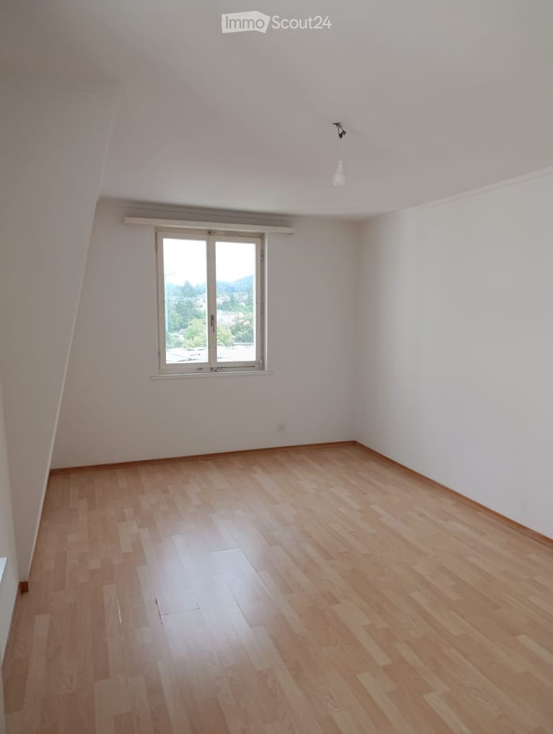 Empty room with wooden flooring, white walls, and a large window offering a view of the outdoors.