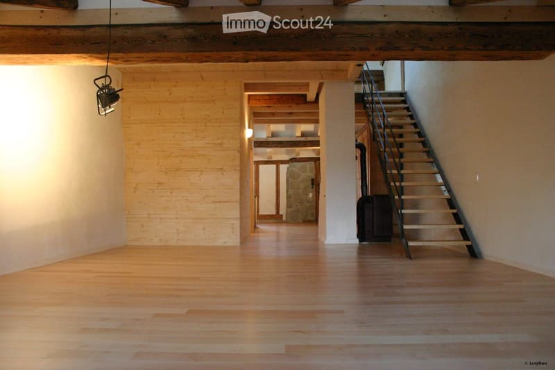 Empty hallway with wooden floors, exposed wooden beams, and a staircase leading upwards.