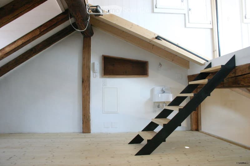 An attic space with exposed wooden beams, a small staircase leading up, a built-in shelf, and a small sink in the corner.