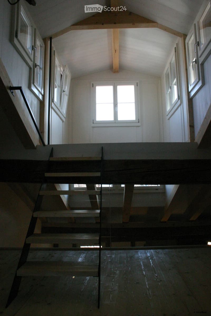 Modern hallway with wooden flooring, glass railing, and multiple windows allowing natural light to fill the space.