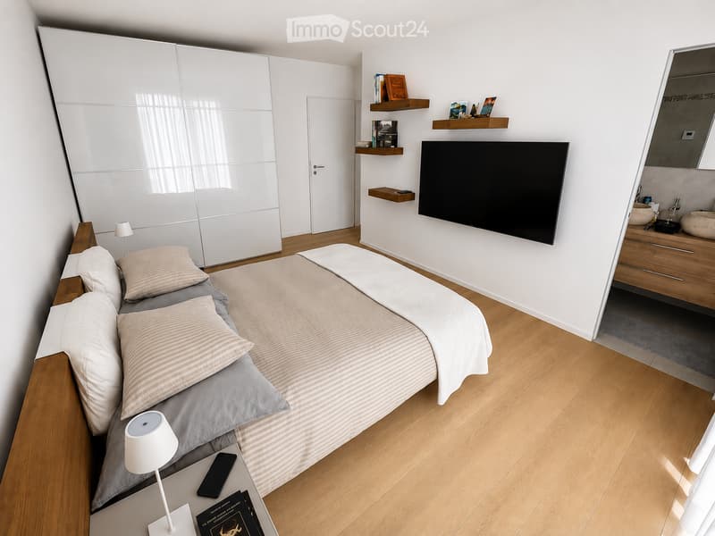 Modern bedroom with a large bed, nightstand, lamp, television, wardrobe, shelves with books, and a small bathroom area with a sink and mirror.