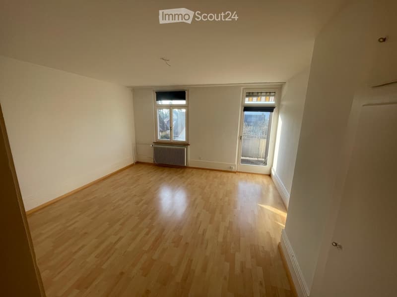 Empty room with wooden flooring, white walls, and two windows, one with a radiator below it.