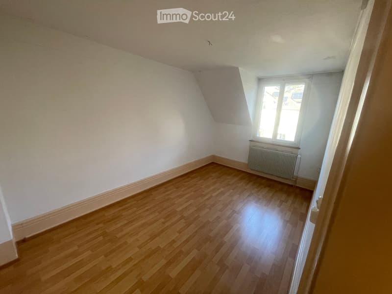 Empty room with wooden flooring, white walls, and a window with a radiator below it.