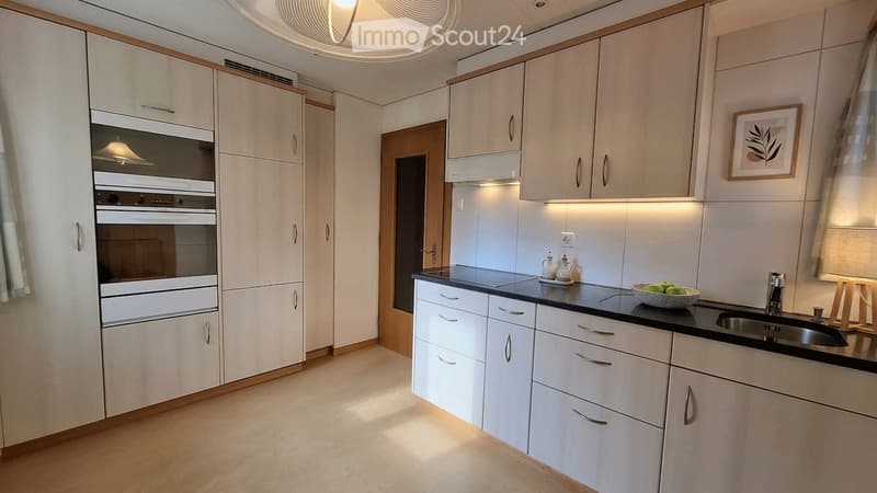 Modern kitchen with white cabinets, built-in oven, black countertop, and a small decorative bowl on the counter.