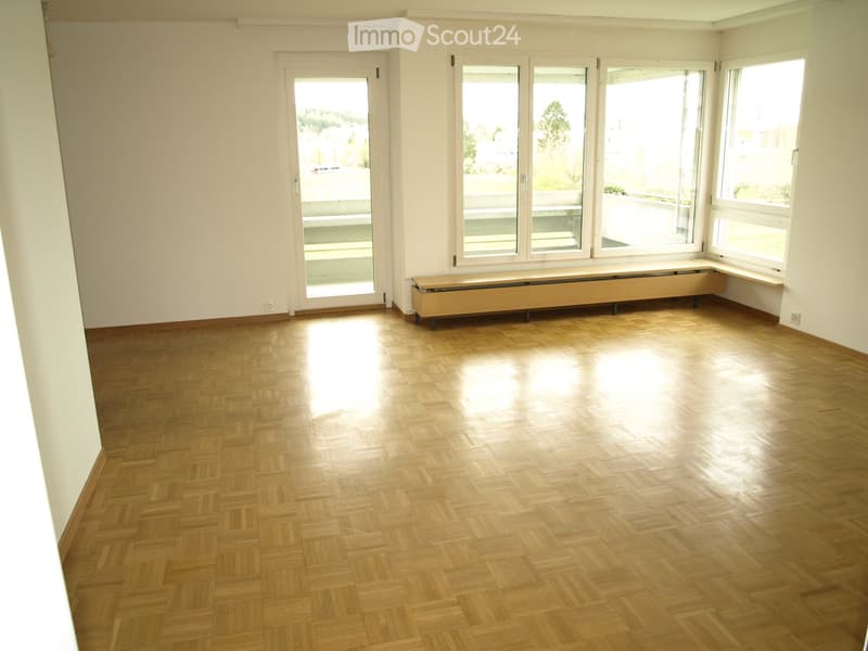 Empty room with wooden herringbone flooring, large windows, and a radiator. No furniture or equipment present.