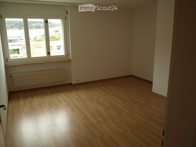Empty room with wooden flooring, large windows, radiator, and neutral-colored walls.