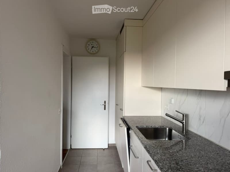 Modern kitchen with white cabinets, granite countertop, stainless steel sink, and a clock above the door.