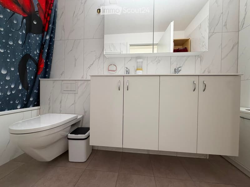 Modern bathroom with white marble tiles, a toilet, a sink with a cabinet, a mirror, and a decorative shower curtain.