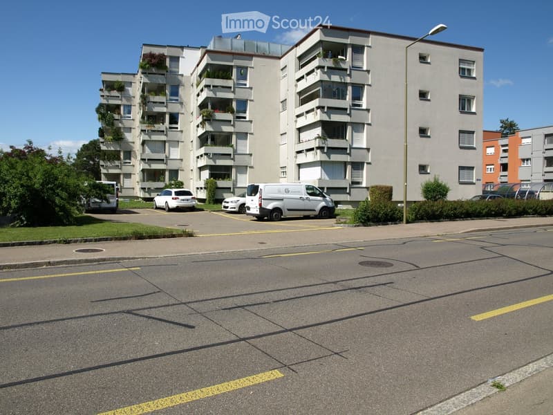 An apartment building with multiple balconies, parking space for several cars.