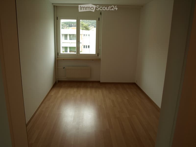 Empty room with wooden flooring, white walls, and a window with a radiator below it.