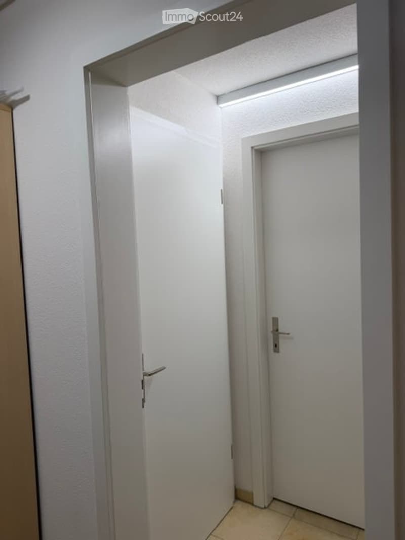 A narrow, well-lit hallway with white walls, a tiled floor, and two white doors with silver handles.