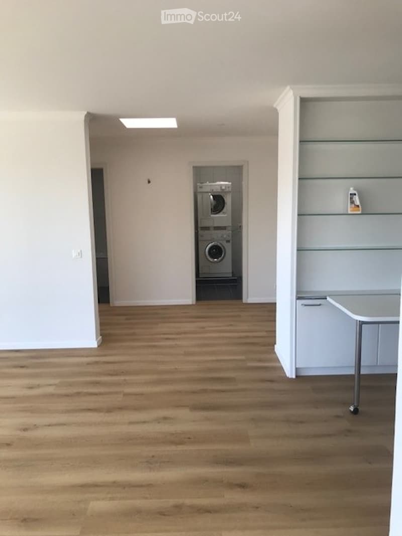 Empty room with wooden flooring, white walls, and a private washing machine in the corner.