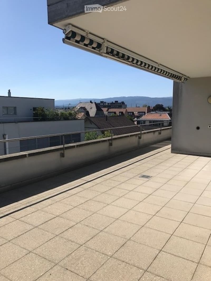 Balcony with tiled floor, metal railing, and a view of the city and surrounding hills.