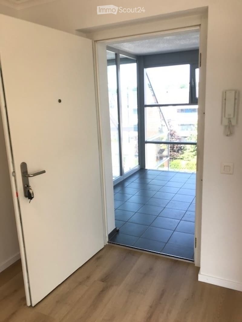 Open doorway leading to a tiled balcony area with large windows and a view of greenery outside.