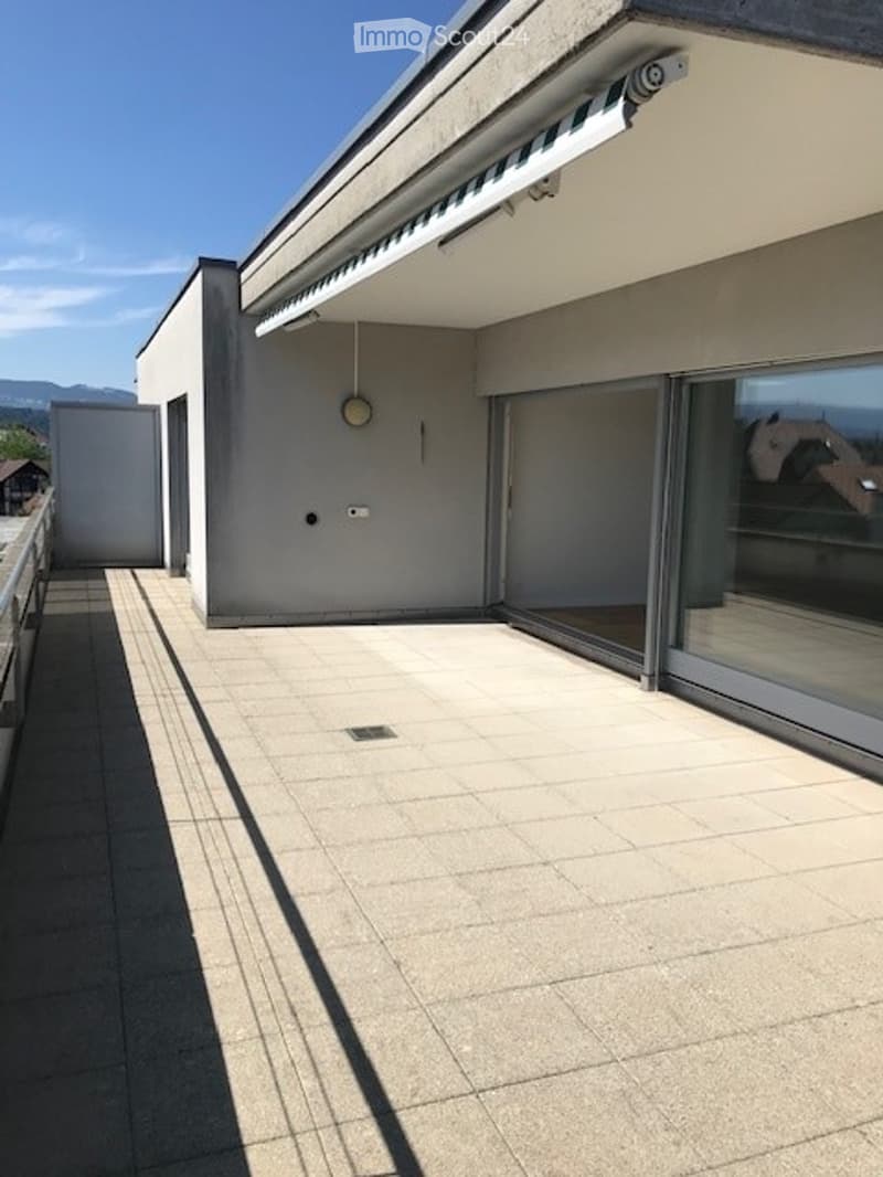 Modern balcony with large sliding glass doors, tiled floor, and a view of the surrounding landscape.
