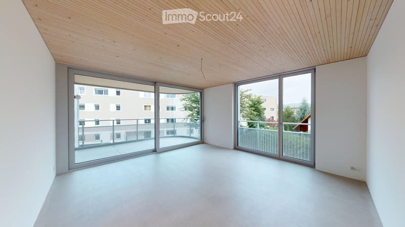 Empty room with white walls, light wooden ceiling, large sliding glass doors leading to a balcony, and a smooth concrete floor.