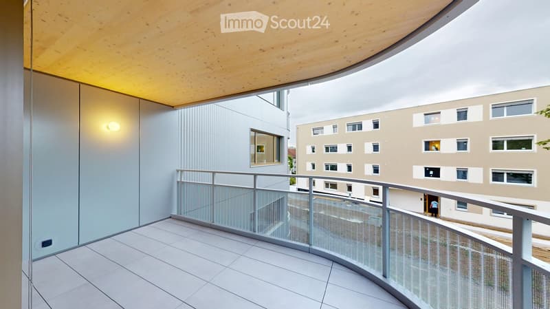 Modern balcony with white tiled floor, glass railing, and wooden ceiling. View of neighboring building with multiple windows.