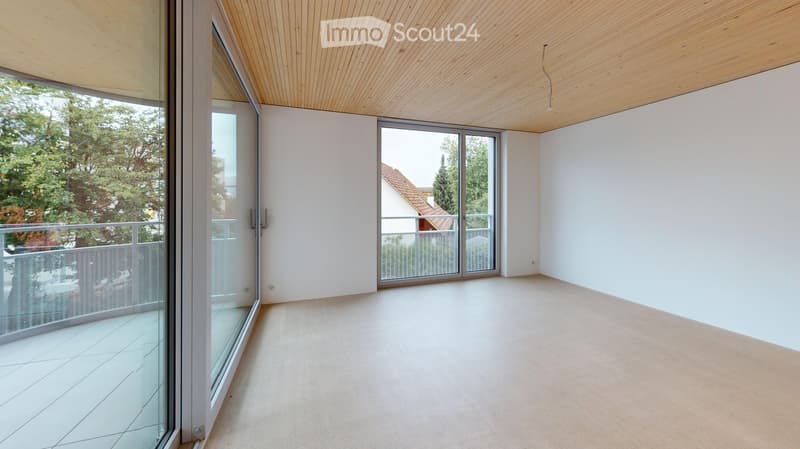 Bright, empty room with white walls, light wooden ceiling, large glass sliding doors leading to a balcony, and a tiled floor.