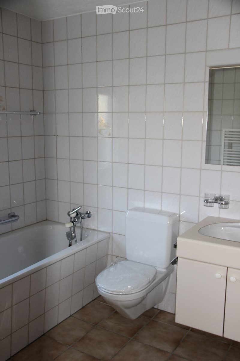 Bathroom with white tiled walls, a toilet, a bathtub, a sink with a mirror, and a faucet.