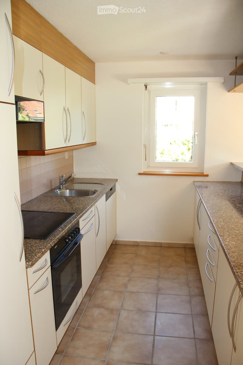 Modern kitchen with light-colored cabinets, granite countertops, stainless steel sink, oven, and dishwasher. Features a window with a view of greenery outside.