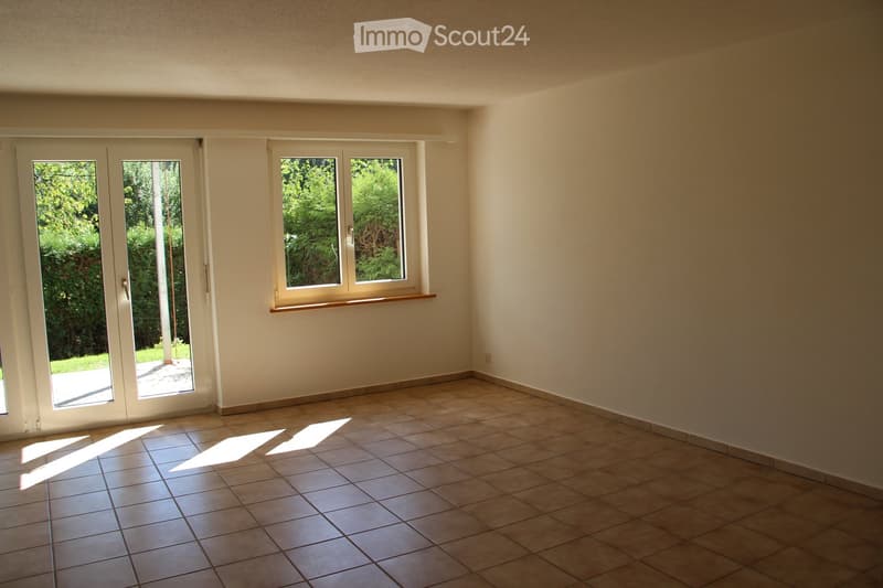 Empty room with tiled floor, large windows, and sliding glass doors leading to an outdoor area.