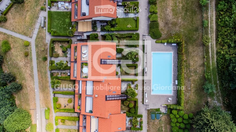 Aerial view of a residential property with a swimming pool, well-maintained garden, and multiple buildings with red-tiled roofs.