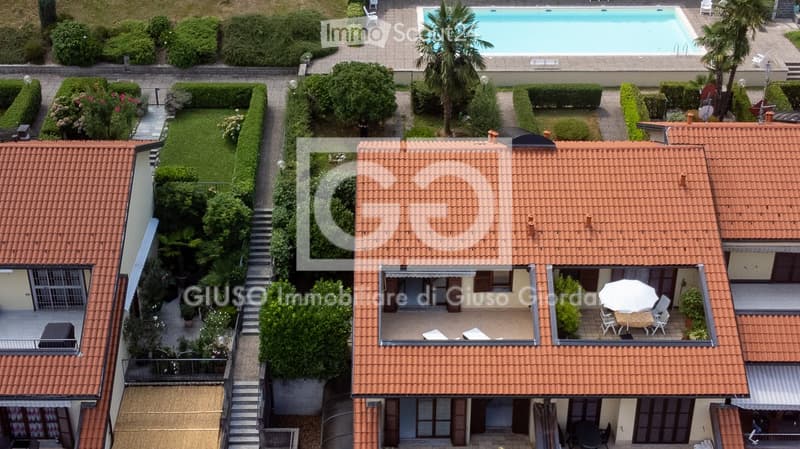 Aerial view of a residential complex with a swimming pool, well-maintained gardens, and outdoor seating areas on the rooftop.