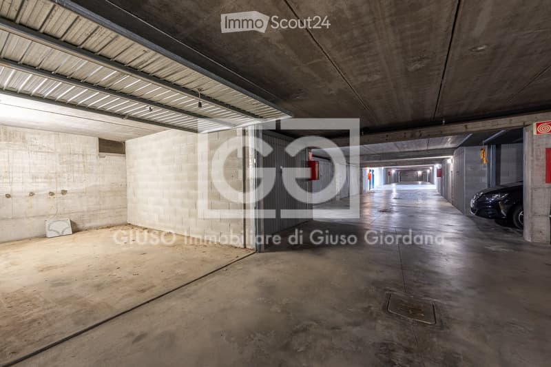 Underground parking area with concrete walls, ceiling, and a parked car visible in the distance.