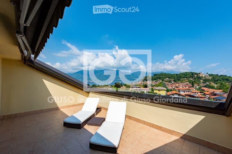 Balcony with sun loungers, tiled floor, and scenic view of a town and mountains.