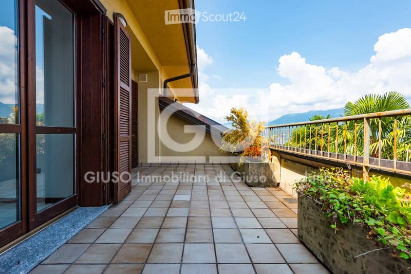 Balcony with tiled flooring, wooden shutters, metal railing, and potted plants, offering a scenic mountain view.