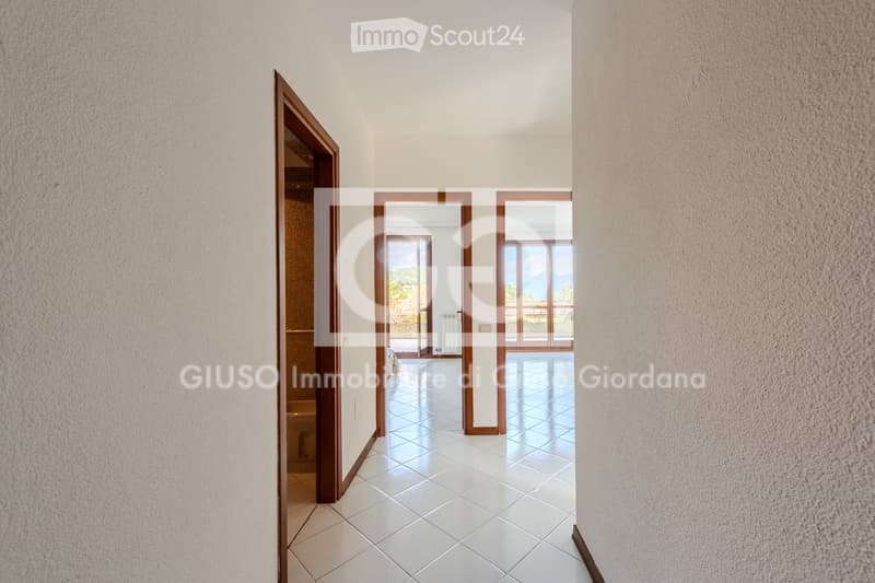 Empty hallway with white tiled flooring, light-colored walls, and several open doors leading to other rooms.