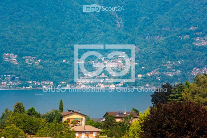A scenic view of a town nestled on a hillside overlooking a lake, surrounded by lush green trees and mountains.