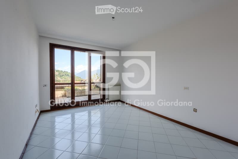 Empty room with white tiled flooring, white walls, and large sliding glass doors leading to a balcony with a scenic mountain view.