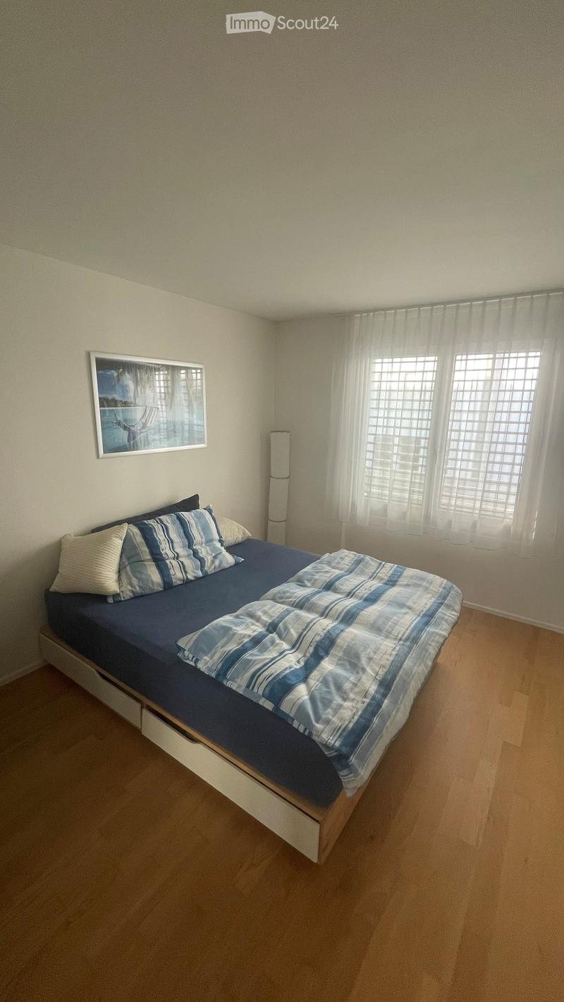 A tidy bedroom with a single bed, blue and white bedding, a picture frame on the wall, and a floor lamp near the window.