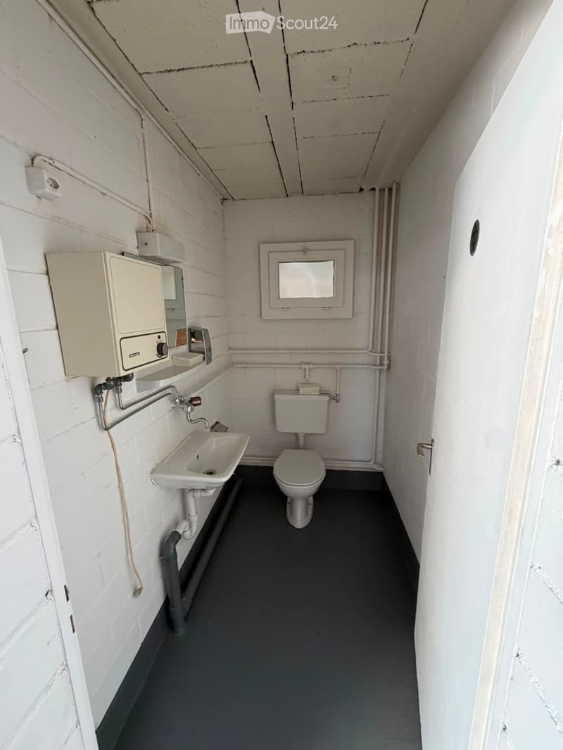 Small bathroom with white brick walls, black floor, toilet, sink, mirror, and water heater.