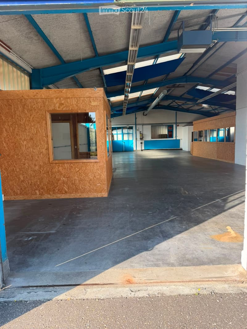 Empty indoor corridor with concrete floor, blue structural beams, and wooden partitions on both sides.