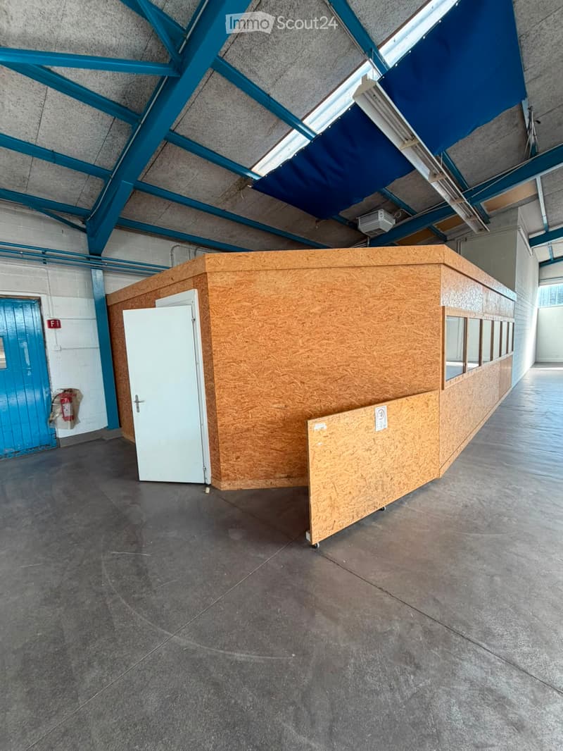 Empty industrial-style room with concrete floor, exposed metal beams, and a small wooden booth with a door and windows.